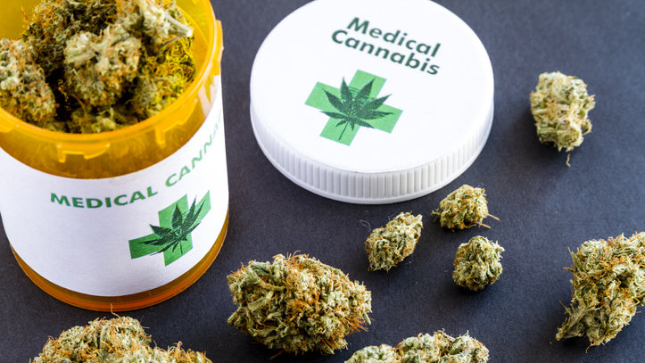 Medical marijuana buds in large prescription bottle with branded cap on black background