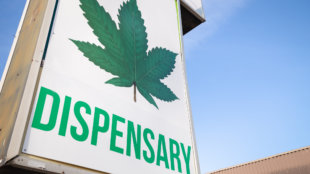 A cannabis dispensary sign with a large marijuana leaf on it
