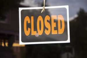 Closed sign hanging in business window by a string - crooked with glob of glue also attaching it to window - some abstract reflections