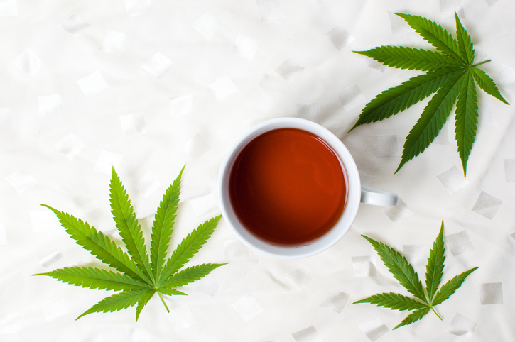 Cannabis tea and marijuana leaves on white fabric top view