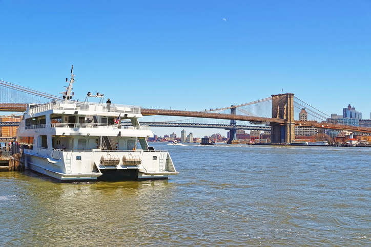 Ferry and and Brooklyn bridge across East River, New York, USA. Brooklyn Bridge is among the oldest bridges in the United States of America. Brooklyn Heights on the right. Tourists on the boat.