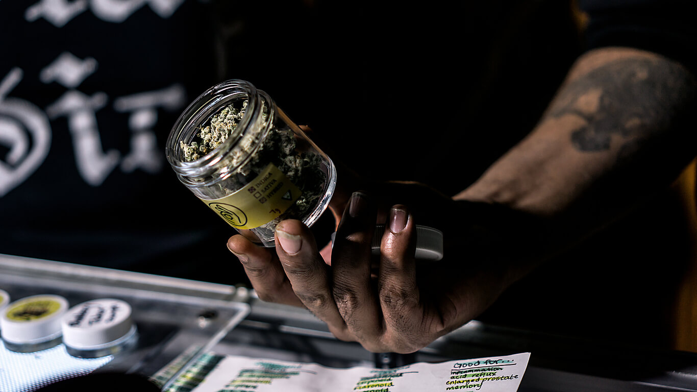 A budtender showing off a jar of cured cannabis flowers.