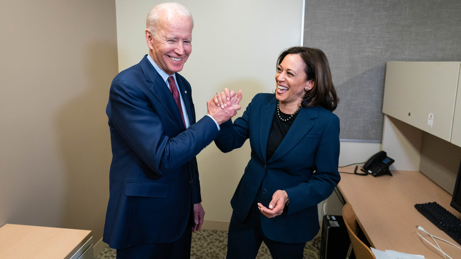 Joe Biden and Kamala Harris holding hands smiling in an office