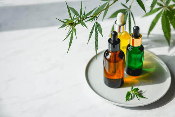 Glass bottles of CBD tinctures on a plate next to hemp leaves