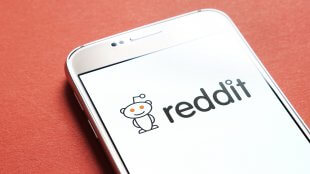 A closeup of the Reddit logo on a mobile phone with an orange background