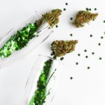 Image of two champagne flutes, green glitter, and four cannabis nugs on a white table.