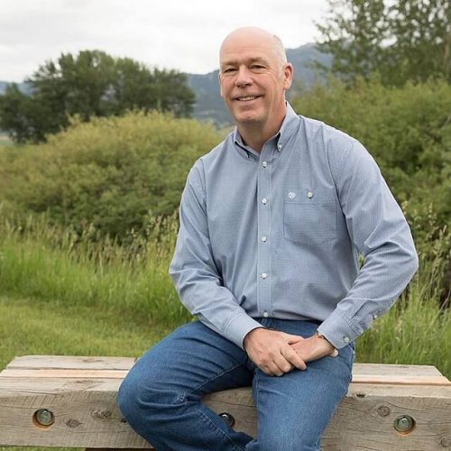 Montana Governor Greg Gianforte sitting on a wooden bench in nature