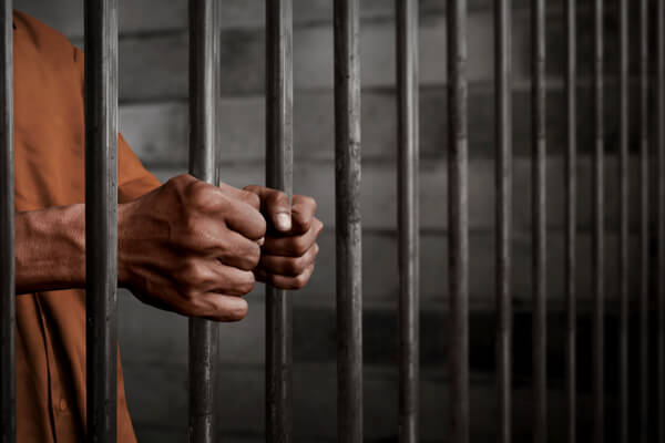 A person in a jail cell with their hands on the bars