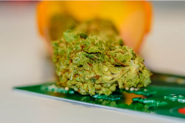 Medical Marijuana lying on top of a credit card with a perscription bottle in the background