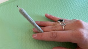 a woman's hand with rings on fingers holds out a rolled Dutch Roll joint