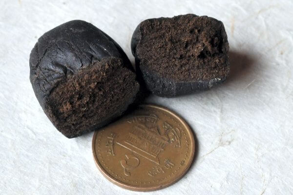 Two dark brown, round balls of hash next to a penny