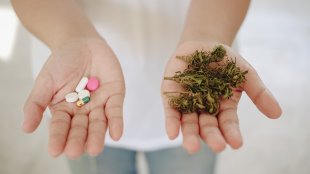 a person holds out both of their hands, one with marijuana and one with a handful of pills