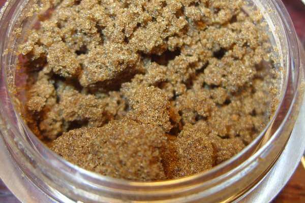 A clear container with tiny brown, micro crystals of cannabis bubble hash inside