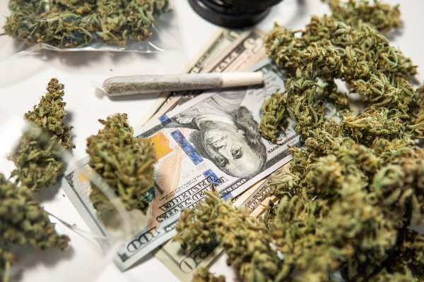 Cannabis buds, money, and joints in a pile.