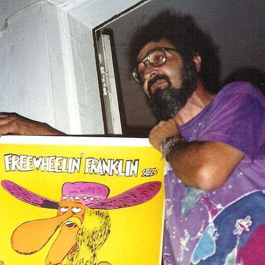 photo of Jack Herer, wearing glasses and a purple shirt, holding up a “Freewheelin Franklin” poster