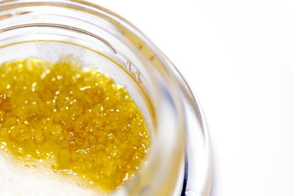 a clear container housing a golden yellow saucy cannabis concentrate with tiny crystals inside