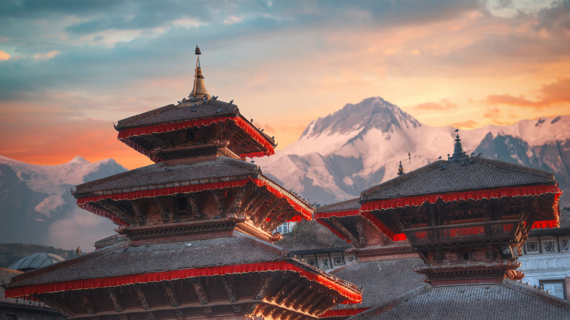 A temple with a pagoda roof in front of a mountain range and orange sunset