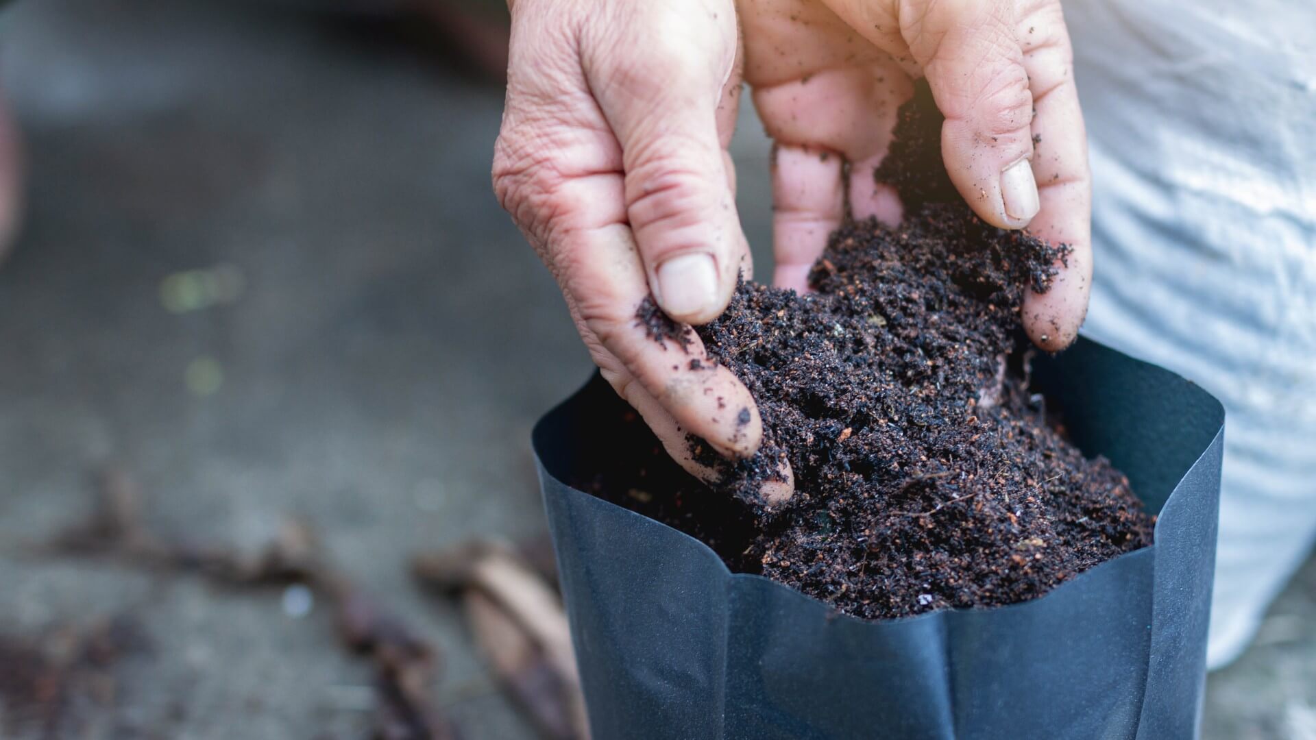 hands pouring soil into a grey fabric pot.