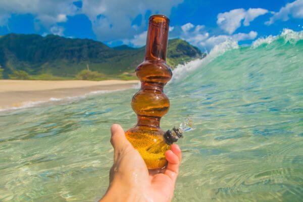 Hand holding bong with ocean waves and Hawaiian island in the background