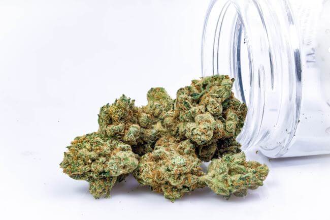 green and orange cannabis buds spilling out of a glass jar