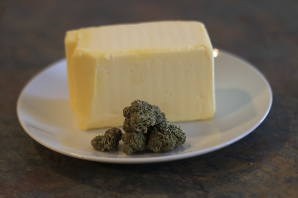 A pound block of yellow butter next to a pile of green cannabis buds.