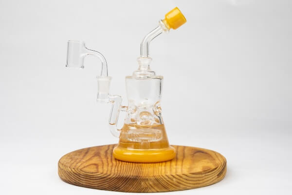 a clear and yellow glass dab rig resting on a wooden block