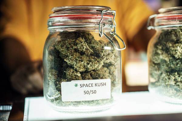 A glass jar filled with green cannabis buds with a label on it that reads space kush.