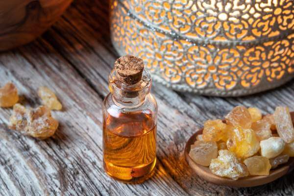 A bottle of orange liquid and cork top with Frankincense resin chunks surrounding it