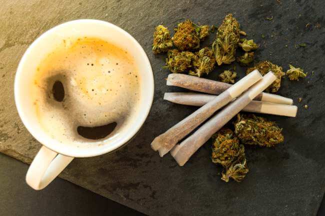 a cup of hot coffee next to four cannabis joints and cannabis nugs